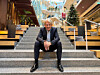 Eivind Roald sits on broad steps inside a modern, plant-filled building with a Christmas tree behind him.