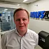 Man in a white shirt posing in a modern office beside a blue wall logo.