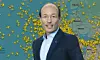 A man in a suit stands in front of a Europe map covered with yellow markers.