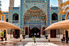 Ornate blue-tiled courtyard with arched entrances, covered walkways and palm trees.