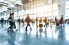 People walk with suitcases through a bright airport terminal concourse.
