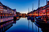 Colourful Nyhavn buildings and boats reflected in a calm Copenhagen canal at twilight.