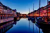 Colourful Nyhavn buildings and boats reflected in a calm Copenhagen canal at twilight.