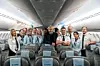 Eivind Roald stands with Norse staff in the aisle of an aircraft cabin with rows of empty seats.
