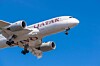 Qatar Airways plane flying low with landing gear down against a blue sky.