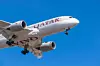 Qatar Airways plane flying low with landing gear down against a blue sky.