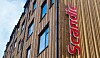 Vertical red Scandic sign mounted on a brown hotel building with rows of windows.