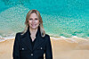 Charlotte Blum in a dark jacket, pictured against turquoise sea and a sandy beach.