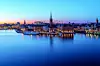 Stockholm waterfront skyline glowing at dusk, reflected in calm blue water.