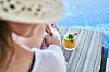 Person sitter vid pool på solstol med färgglad drink bredvid sig.
