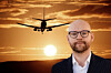 Person i kostym framför siluett av flygplan som landar i solnedgång.