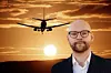 Person i kostym framför siluett av flygplan som landar i solnedgång.