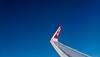 AirAsia-flygplans vinge med röd logotyp mot klarblå himmel.