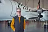 En man står framför ett mindre passagerarflygplan i en hangar.