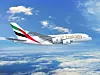 Emirates passenger jet flying above clouds against a blue sky.