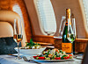 Dukat bord i ett privat jetplan med champagneflaska, glas, sallad och fönster i bakgrunden.