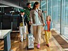 En familj går med en resväska genom en ljus flygplatsterminal bredvid stora fönster.