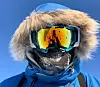 Close-up of a person wearing a blue winter jacket and mirrored ski goggles with fur-lined hood.