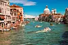 Båtar kör på en kanal i Venedig med historiska hus och en kyrkobyggnad i bakgrunden.