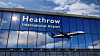 Heathrow International Airport sign and aircraft reflected in a glass terminal façade.