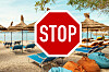 Röd STOPP-skylt framför solstolar, parasoller och säckstolar på en strand.