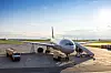 Passagerarflygplan parkerat på flygplatsens ramp med ett fordon bredvid.