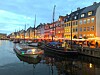 Upplysta husfasader längs en kanal med båtar förtöjda vid kajen i skymningsljus.
