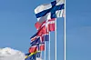 Alla de nordiska flaggorna från Finland, Danmark, Island, Norge och Sverige vajar på höga master mot blå himmel och moln.