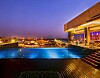 Upplyst pool vid ett modernt hotell med stadsbelysning i bakgrunden vid skymning.