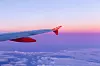 Flygplansvinge med röd vingspets ovanför moln vid solnedgång.