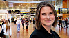 Woman standing in the foreground at a busy Copenhagen Airport terminal with passengers and departure boards behind her.