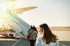A woman walks towards an aircraft on the airport tarmac near the boarding stairs.