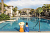 Two people sit by a hotel pool with mountain views at a sunny resort.