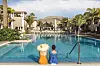 Two people sit by a hotel pool with mountain views at a sunny resort.