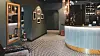 Hotel reception area with patterned floor, curved blue desk, dark walls and warm pendant lighting.