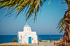 A white seaside chapel framed by palm trees beside the blue Mediterranean in Cyprus.