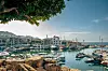 småbåtshamn med fritidsbåtar, hotell, berg och klippor vid en solig kust.