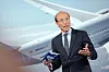 Man i kostym talar framför ett SAS-flygplan och håller dokument i handen.