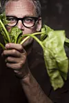 Stefan Eriksson wearing glasses peers through leafy green vegetables against a dark background.