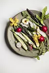 Overhead view of an artfully plated vegetable dish with egg, radishes, greens and edible flowers.