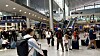 Resenärer med bagage rör sig genom en ljus och välbesökt flygplatsterminal.