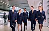 Sex flyganställda i mörkblå uniformer går tillsammans genom en flygplatsterminal.