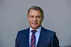 Portræt af Hallvard Bratberg i mørkt jakkesæt og slips foran en grå baggrund.