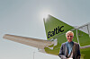 Man standing beside a green and white airBaltic aircraft under a pale sky.