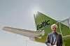 Man standing beside a green and white airBaltic aircraft under a pale sky.