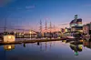 Gothenburg harbour at dusk, with boats, cranes and illuminated buildings reflected in calm water.