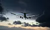 Passagerarflygplan sett framifrån i luften mot mörka moln och en ljus kvällshimmel.
