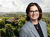 Erika Ståhl wearing glasses and a grey blazer, with rolling countryside behind her.