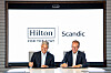 Chris Nassetta and Jens Mathiesen sign documents beneath Hilton and Scandic logos.