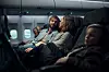 Flera passagerare sitter i säten i en mörkt belyst flygplanskabin.